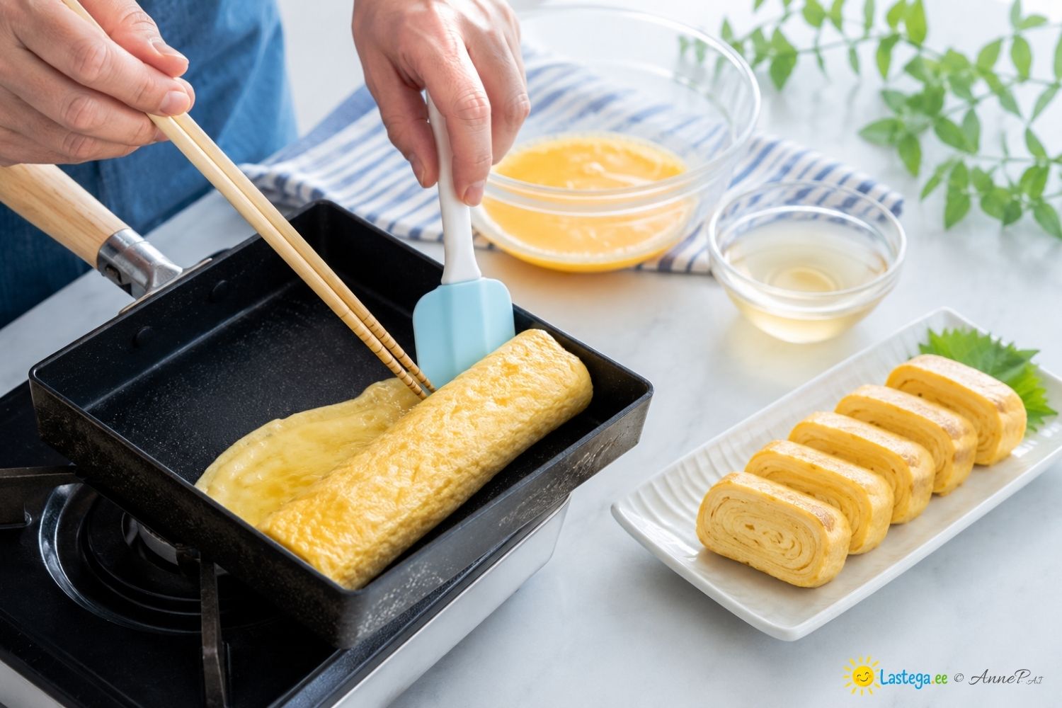 Täiskasvanu rullib kandilisel pannil õhukesi munakihte tamagoyaki’ks, kõrval on viilutatud kihiline rullomlett.