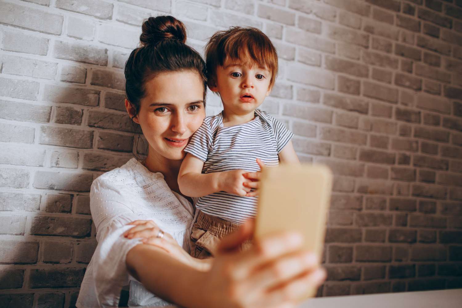 Ema hoiab väikest last süles ja vaatab koos temaga nutitelefoni kaamerasse enne foto internetis jagamist.